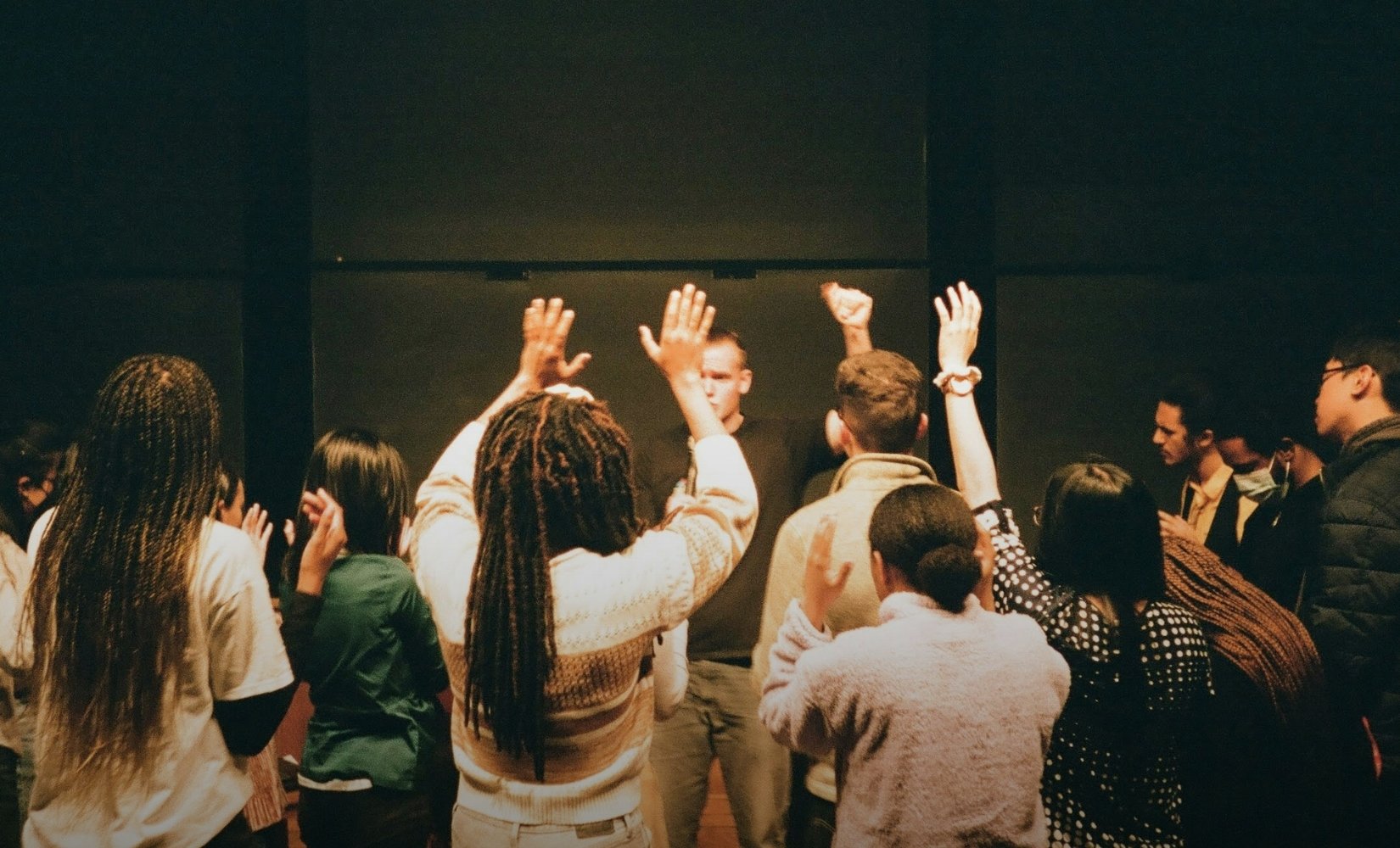 Showing the backs of a group of Gen Z students with hands raised in the air at a worship service at church.