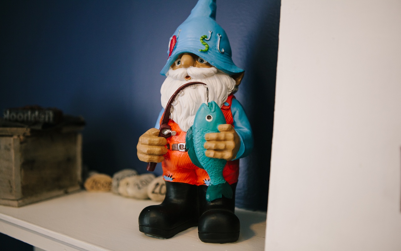 A whimsical gnome statue, equipped with a fishing rod and a fishing pole, is setting on a desk in an office setting.