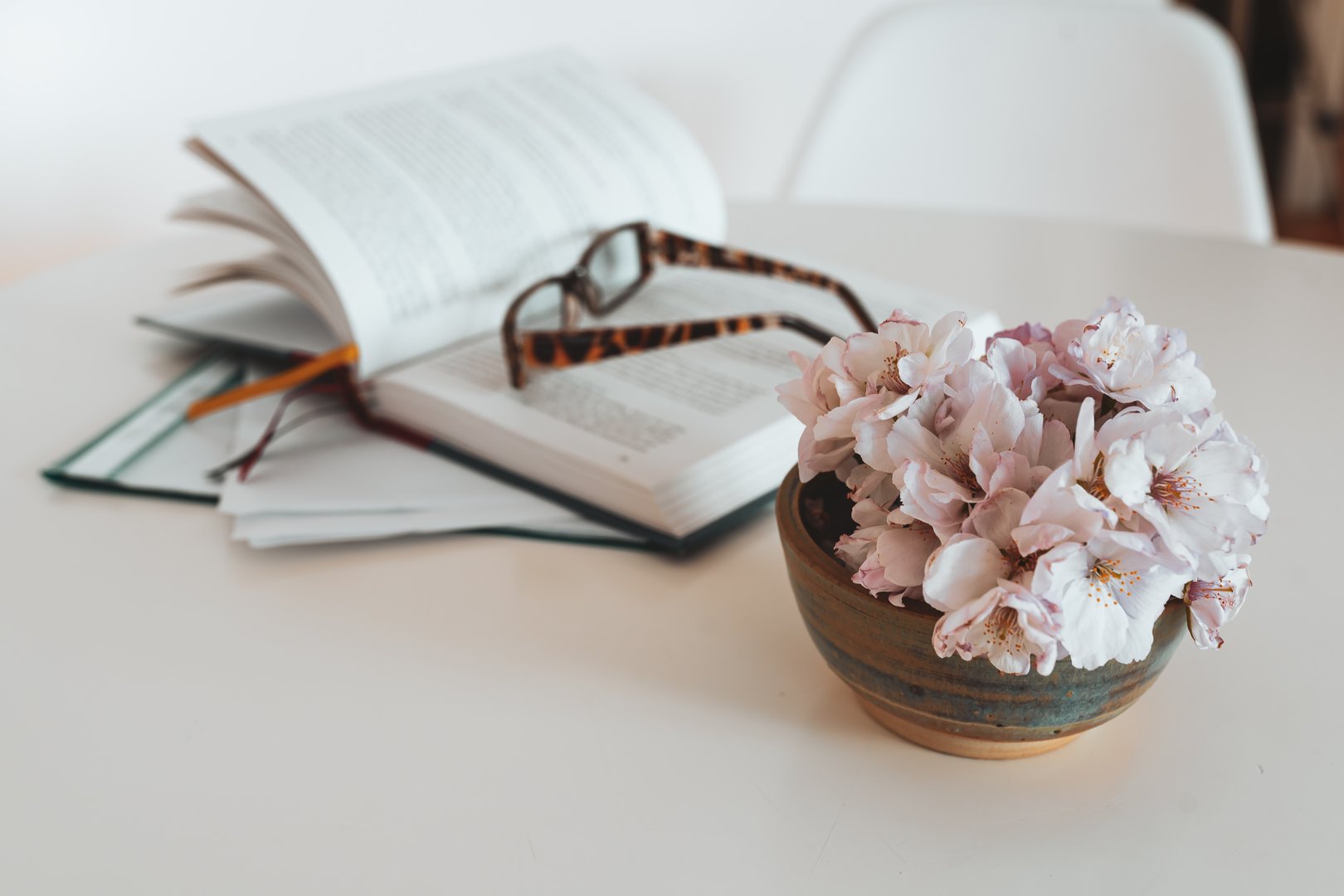a vase of pink flowers beside an open Bible on a wooden table, creating a cozy and inviting atmosphere.